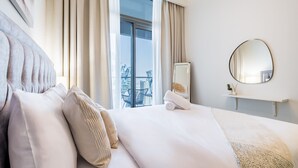 Hotellihuone, jossa on suuri sänky, pyöreä peili, pieni hylly ja ikkunasta avautuva näkymä kaupunkiin.