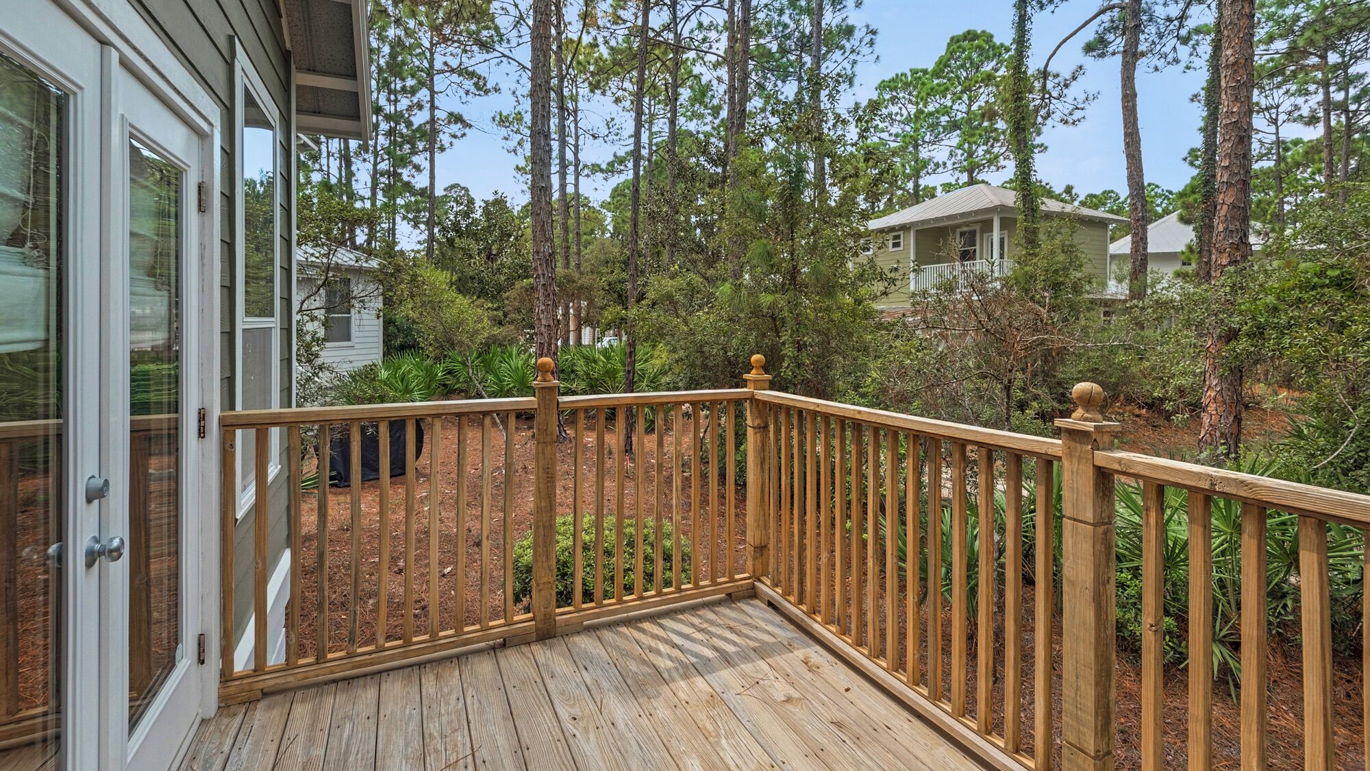 Une terrasse en bois avec une rambarde, entourée d’arbres et avec une maison en arrière-plan.