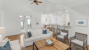 Un salon spacieux avec un canapé blanc, des fauteuils en osier et une table basse en bois.