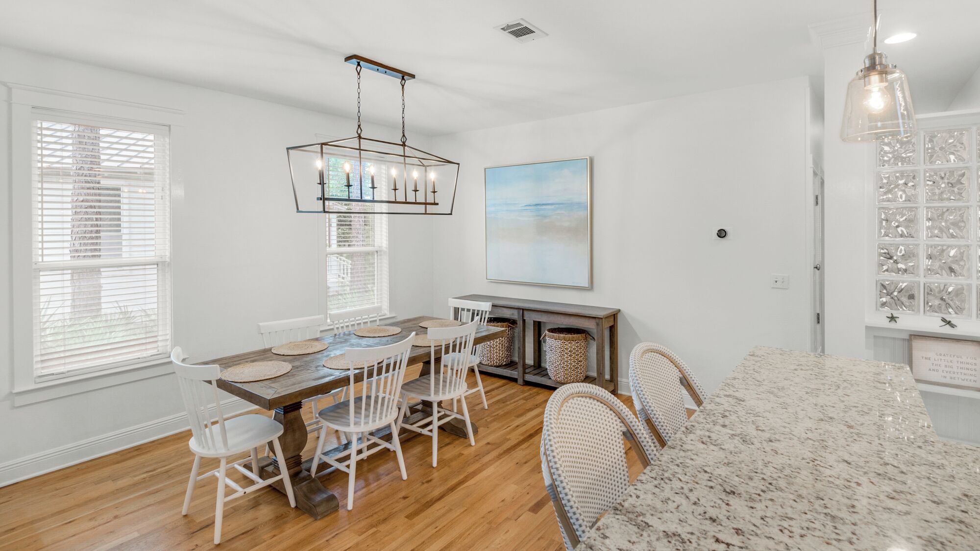 A dining area with a wooden table, white chairs, and a hanging light fixture.