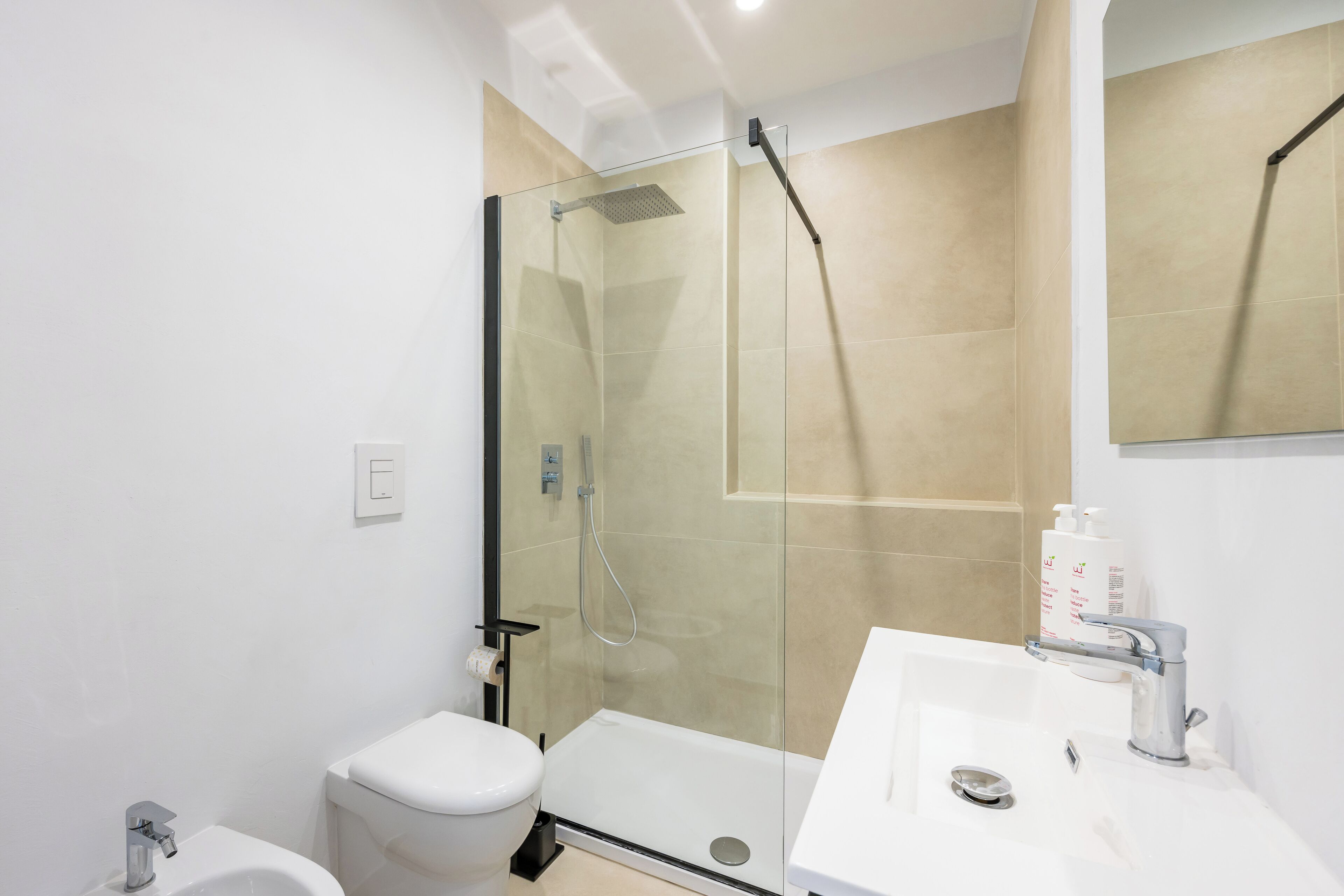 Une salle de bain moderne avec une douche à parois de verre, des toilettes blanches et un lavabo avec un miroir.
