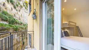 A room with a bunk bed, a window with a view of a stone wall and greenery, and a small balcony with a railing. - Montesanto View Rooms by Wonderful Italy (Naples)