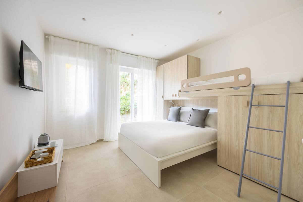 A modern bedroom with a bed, a TV, a wooden wardrobe, and a window with curtains.