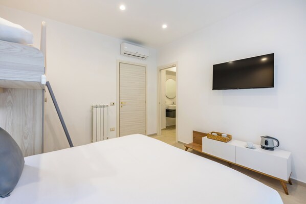 Een moderne hotelkamer met een bed, een aan de muur bevestigde televisie, een nachtkastje met een waterkoker en uitzicht op de badkamer.