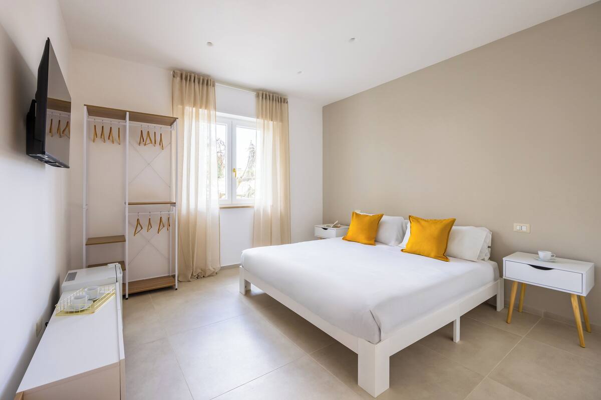 A bedroom with a large bed, a bedside table, a wardrobe, and a window with curtains.