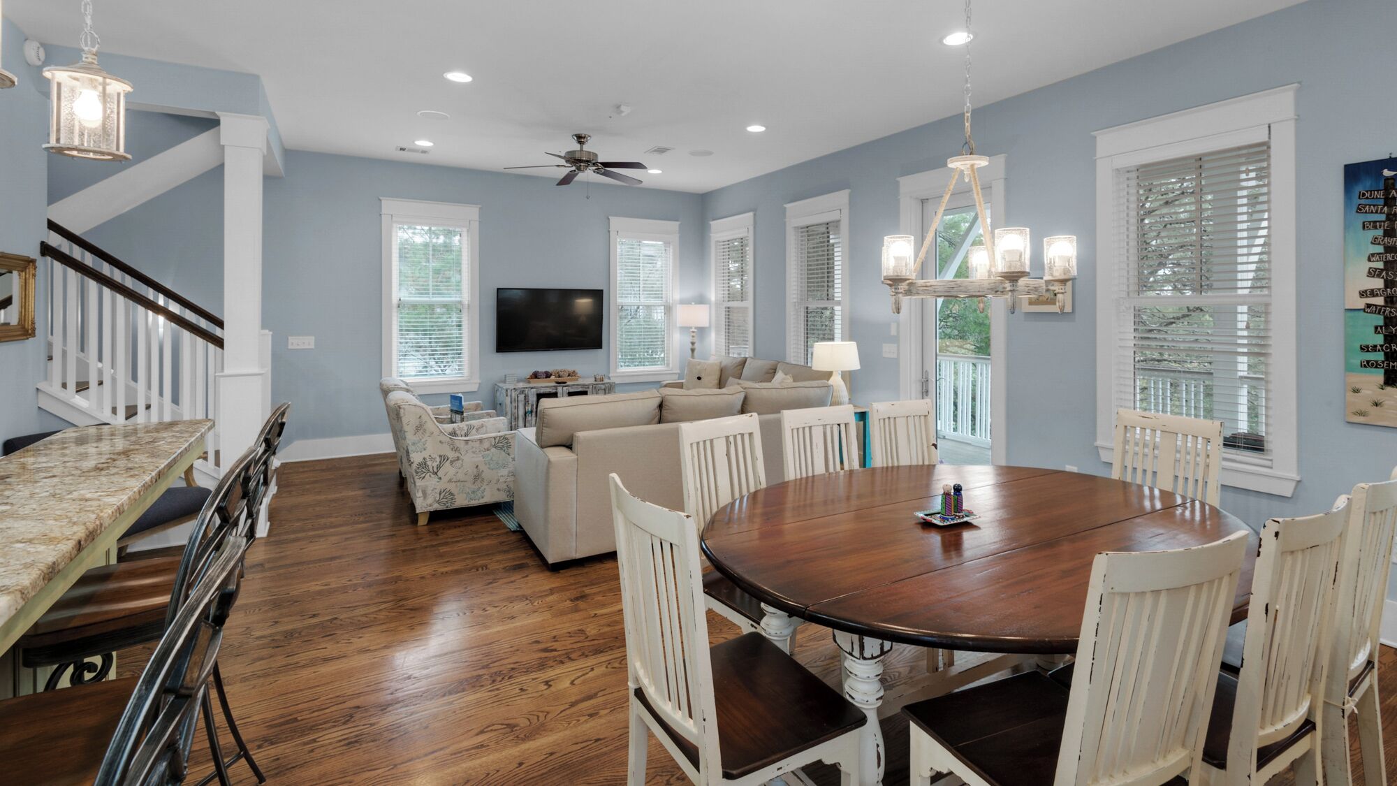 A spacious living room with a large wooden dining table, a sofa, and a TV mounted on the wall.