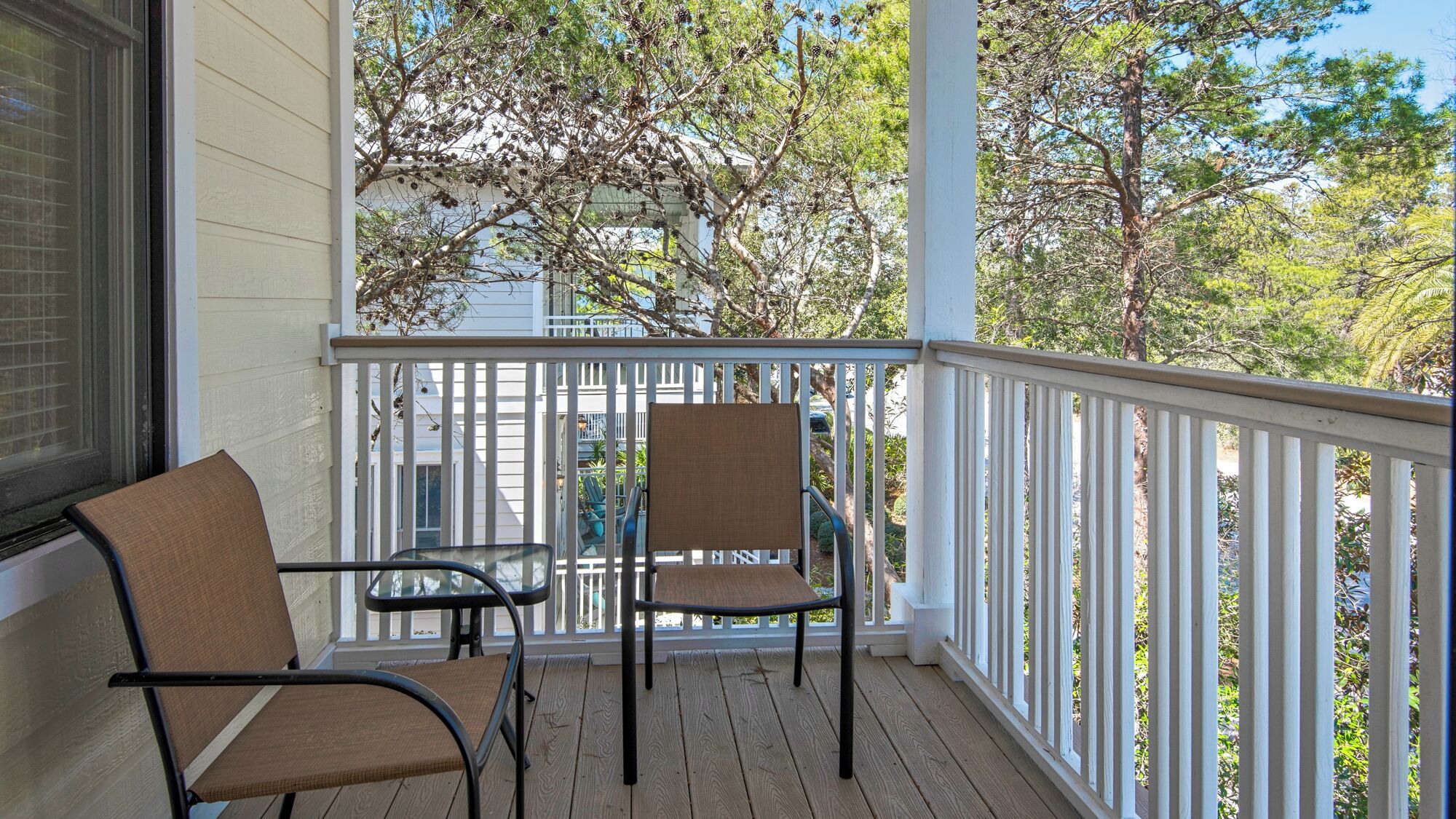 A wooden deck with two chairs and a table, overlooking a residential area with trees and a house.