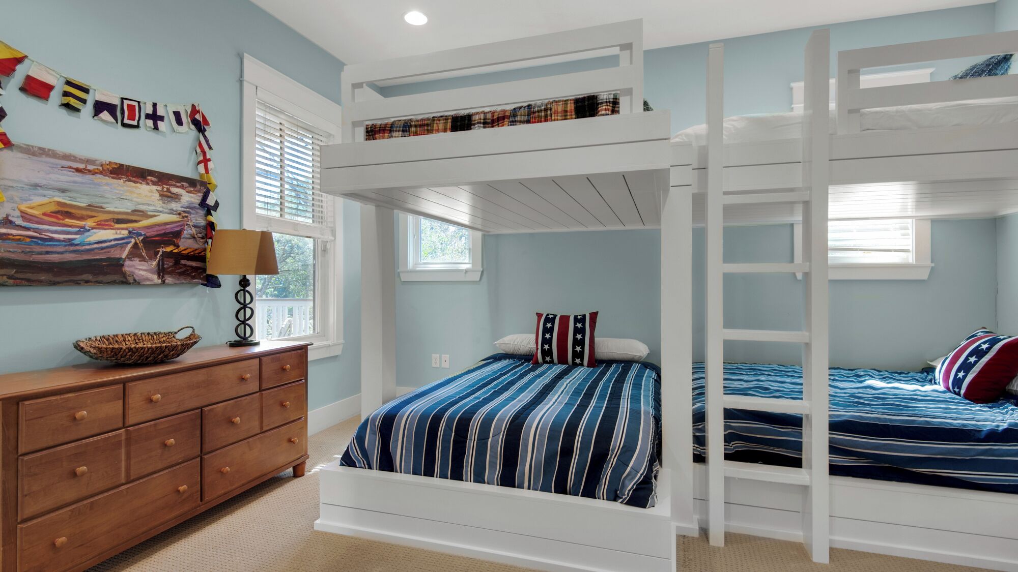 A bunk bed room with a wooden dresser, a lamp, and a painting on the wall.