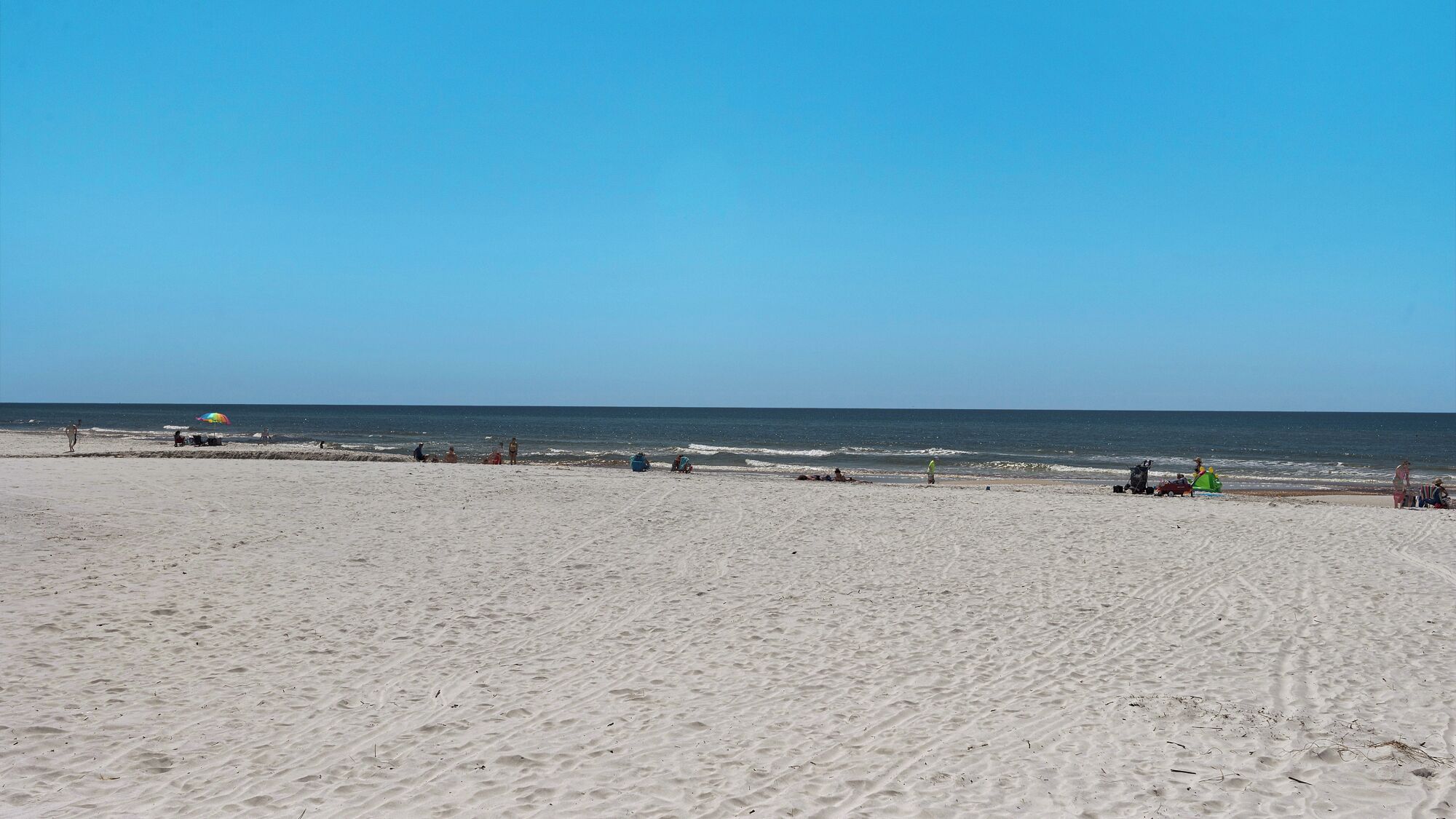 A wide sandy beach with a clear sky and calm sea.