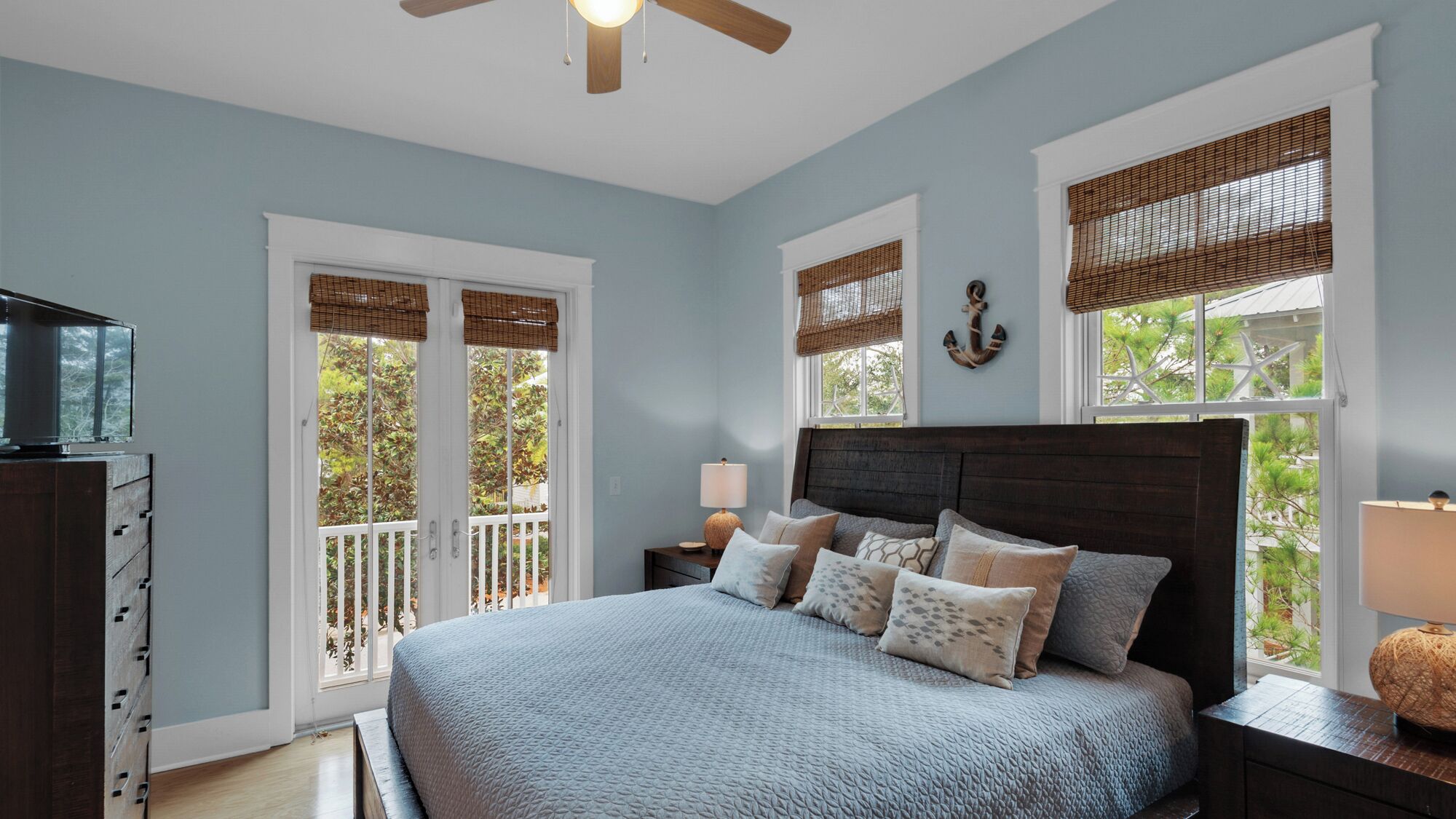 A bedroom with a large bed, two bedside tables, a ceiling fan, and windows with blinds.