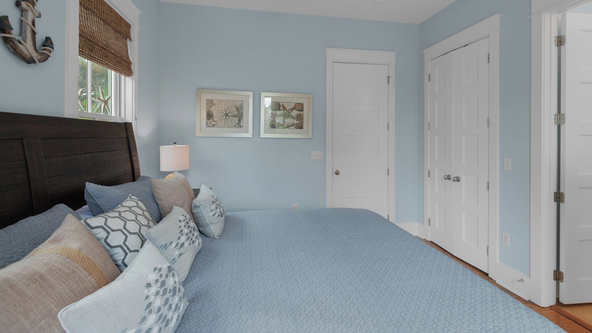 A bedroom with a bed, pillows, a nightstand, a lamp, and two framed pictures on the wall.