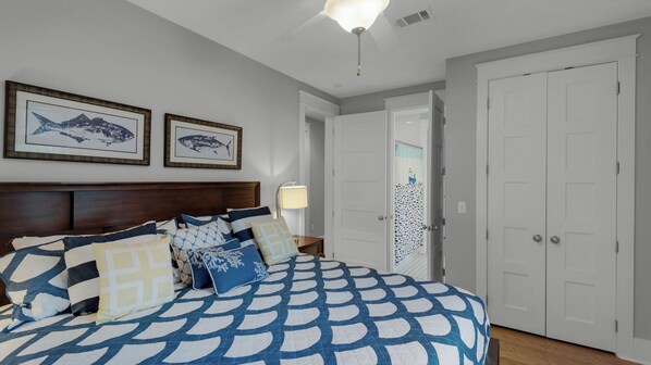 A bedroom with a bed, two framed fish pictures, a nightstand, a lamp, and a door.