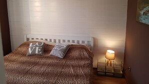 Un dormitorio con cabecera blanca, cama con colcha de estampado de leopardo y dos almohadas con el texto 'LOVE', además de una lámpara de noche.