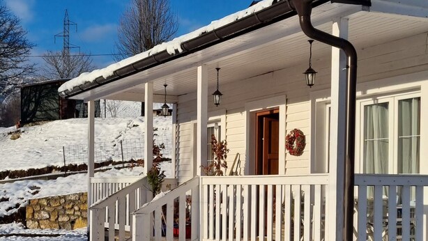 Una casa blanca con un porche, un muro de piedra y un patio cubierto de nieve.
