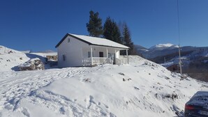 Una casa blanca con porche, rodeada de colinas y montañas cubiertas de nieve.