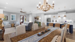 A spacious living room with a large wooden dining table, comfortable seating, a chandelier, and a kitchen area with modern appliances. - Grayton Beach - Gated Community With 2 Pools & Tennis (Santa Rosa Beach)