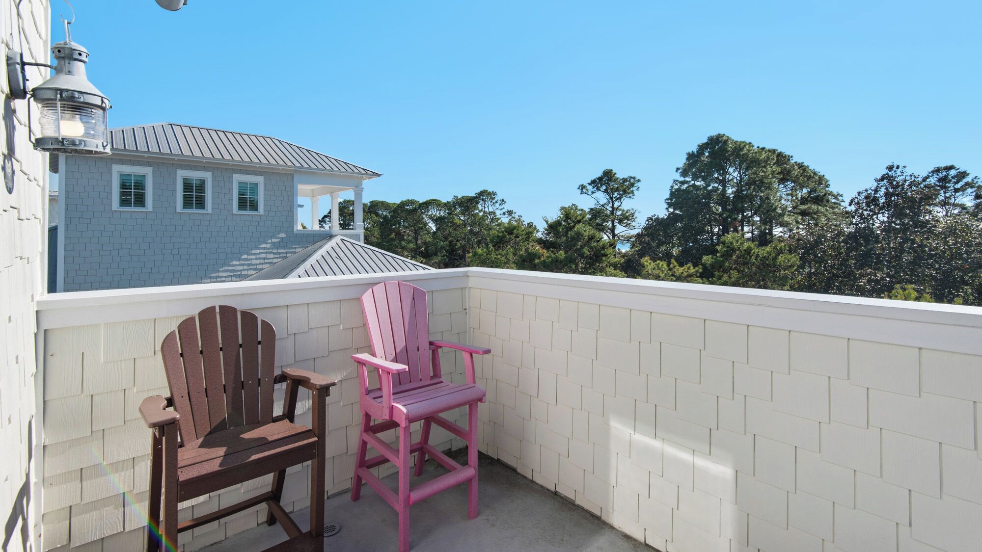 Un balcon avec deux fauteuils Adirondack, une clôture blanche et une maison en arrière-plan.