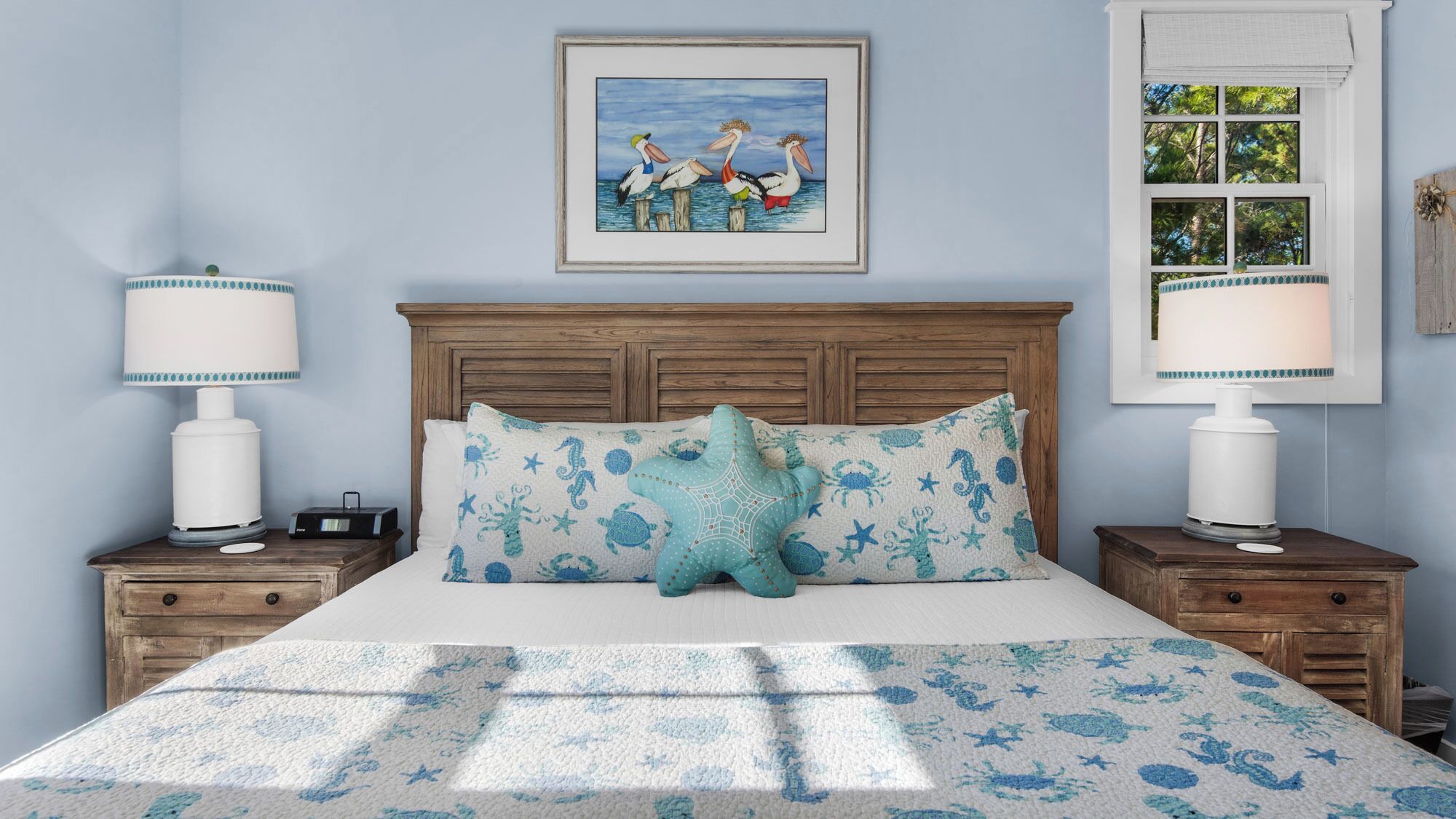 A bedroom with a wooden headboard, a bed with a starfish pillow, matching lamps, and a framed picture of pelicans on the wall.