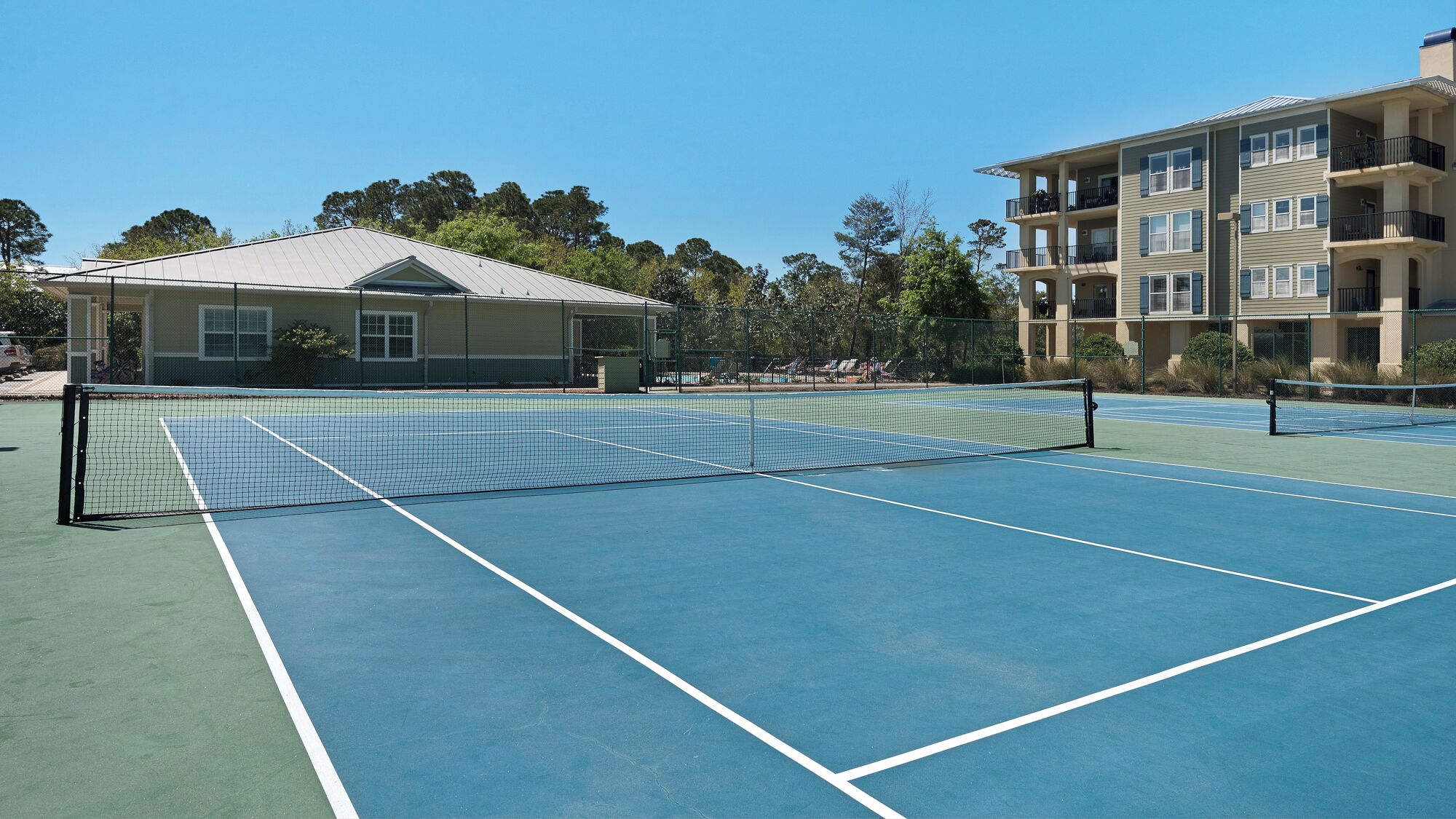 A tennis court with a net, surrounded by a fence, and adjacent to a building with multiple balconies.