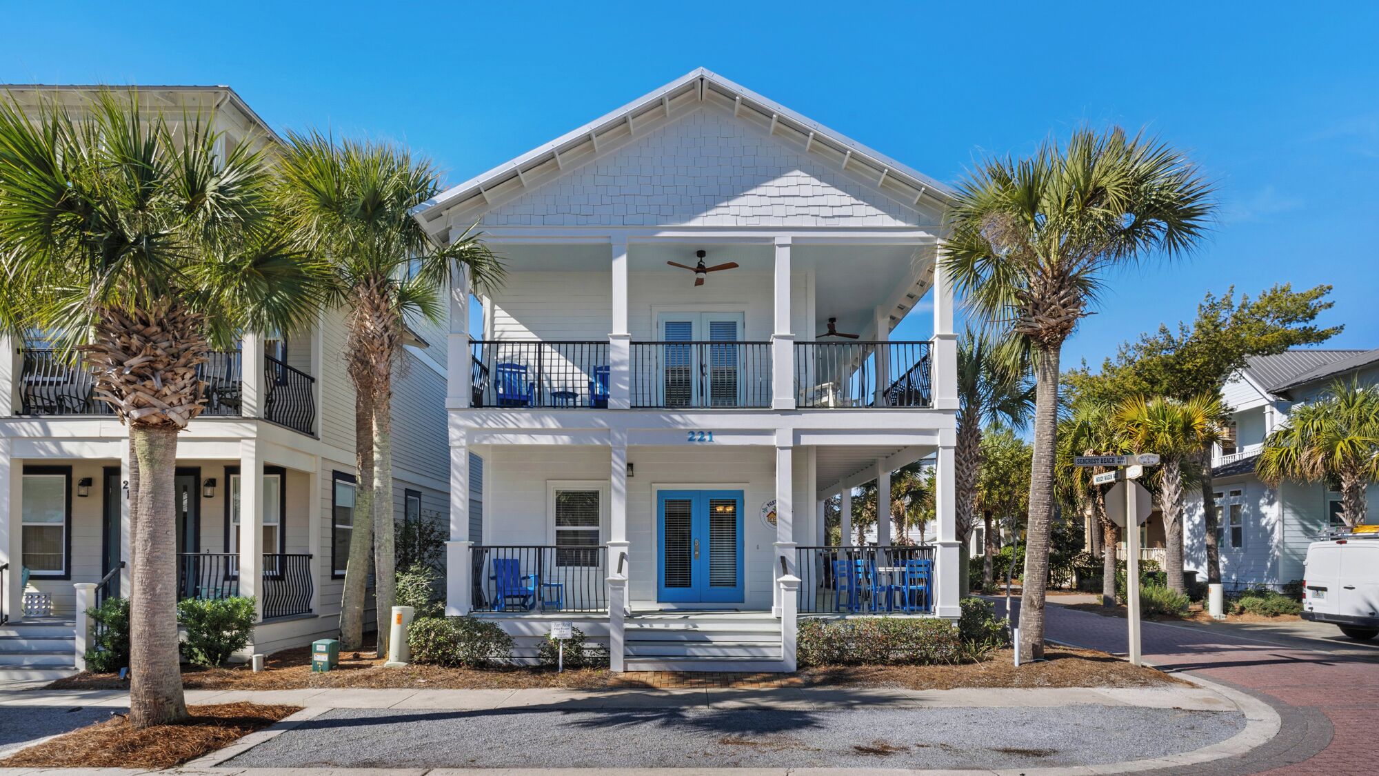 A two-story house with a balcony, a blue door, and a number 221 sign.