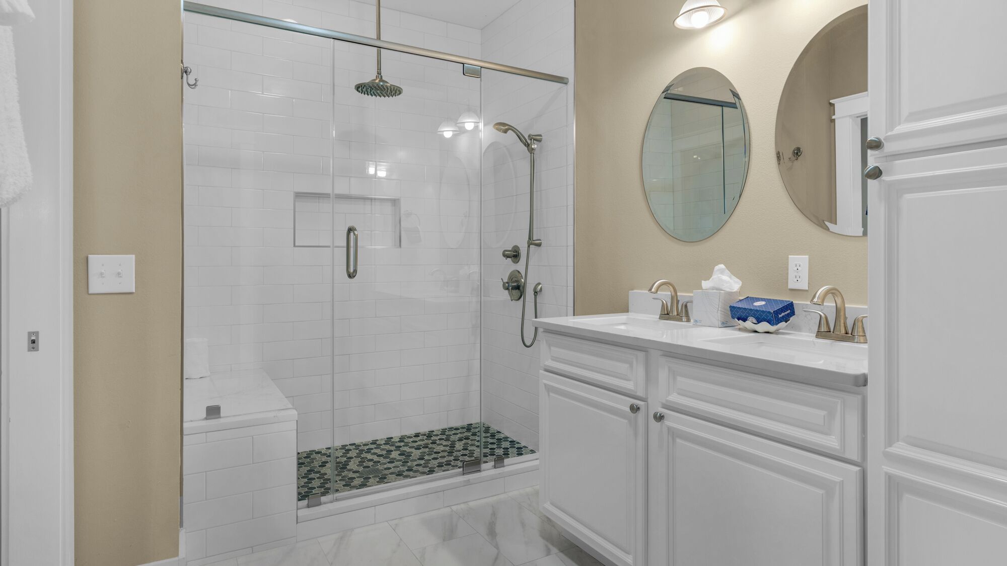 A modern bathroom with a glass-enclosed shower, white vanity with gold fixtures, and a round mirror above the sink.