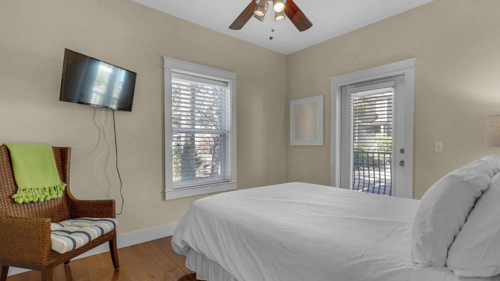 A bedroom with a bed, a television mounted on the wall, and two windows with blinds.