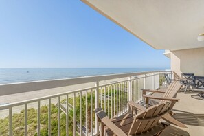 A balcony with a view of the ocean, wooden chairs, and a table.