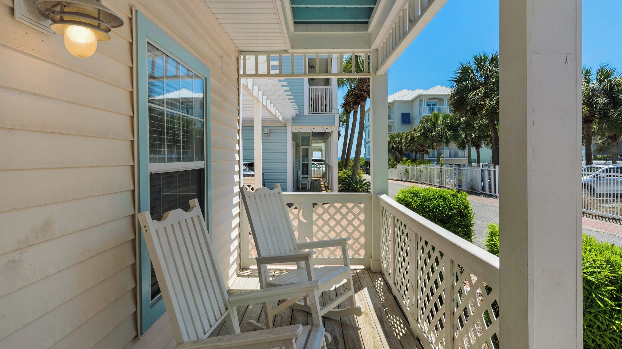 A porch with two white Adirondack chairs, a white railing, and a view of a blue building with a balcony.