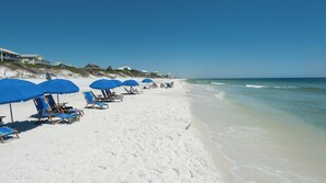 A beach with rows of blue umbrellas and lounge chairs, a sandy shore, and ocean waves. - Great Gulf-side Views - Free Seasonal Beach Chairs! (Santa Rosa Beach)