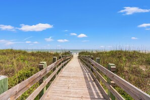 A wooden boardwalk leading to the beach, surrounded by grassy dunes.
