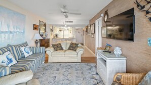 Un salon avec un canapé, une table basse et un tapis. On y trouve également un ventilateur de plafond et un téléviseur fixé au mur.