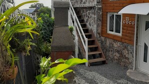 Un bâtiment à deux étages, doté d’une façade en pierre et d’un niveau supérieur en bois. Un escalier mène à l’étage supérieur, et une enseigne indique : « KONTAN WÈ ZOT ».