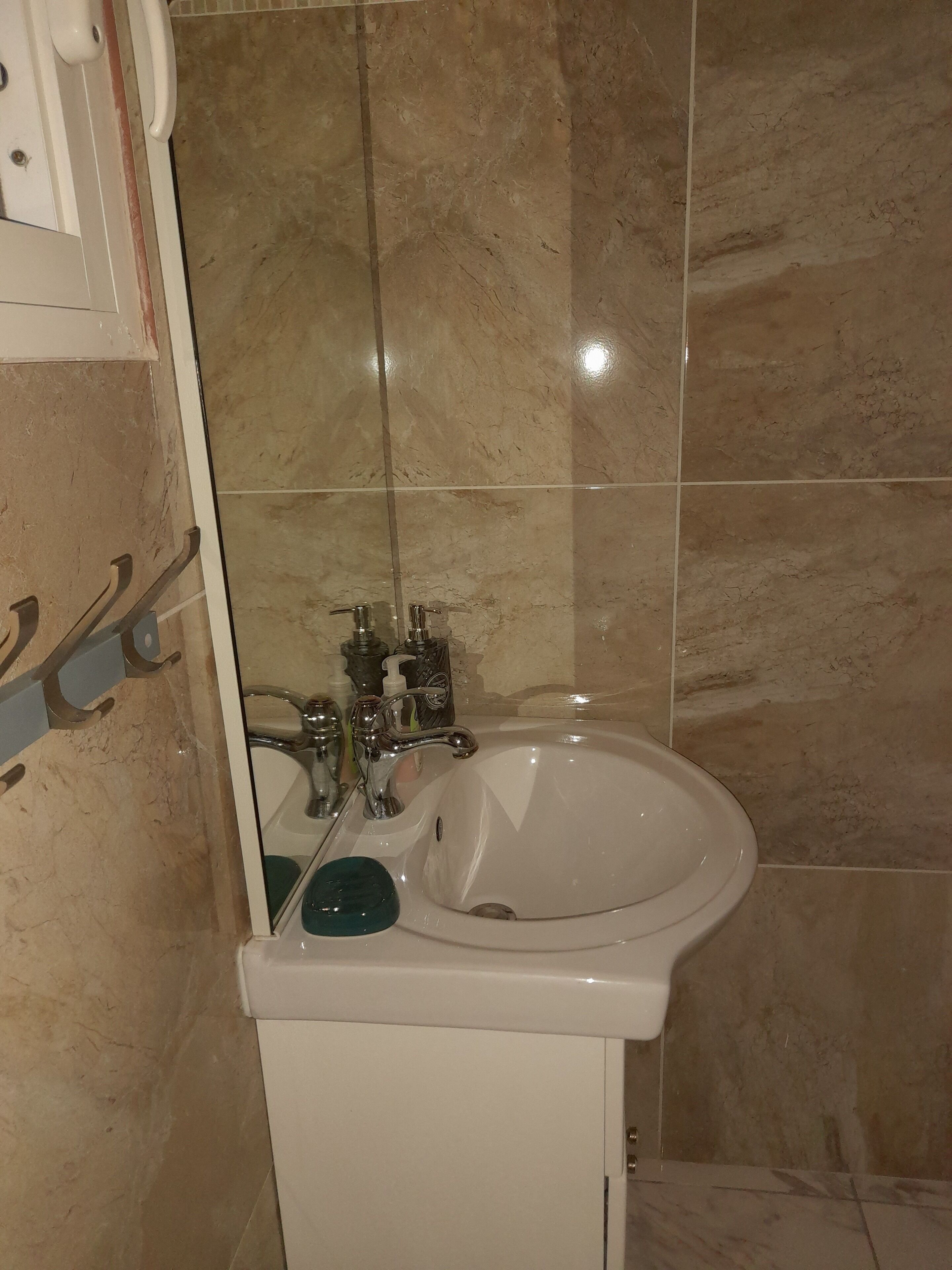 Un baño con lavamanos blanco, un espejo y un perchero para toallas.