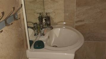 Un baño con lavamanos blanco, un espejo y un perchero para toallas.