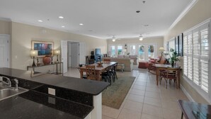 A spacious kitchen with a large island, a dining area with a table and chairs, a living room with a sofa and a TV, and a view of the outdoors through large windows. - Gulf Front in Seagrove - Amazing Views - Easy Beach Access, Pool (Santa Rosa Beach)