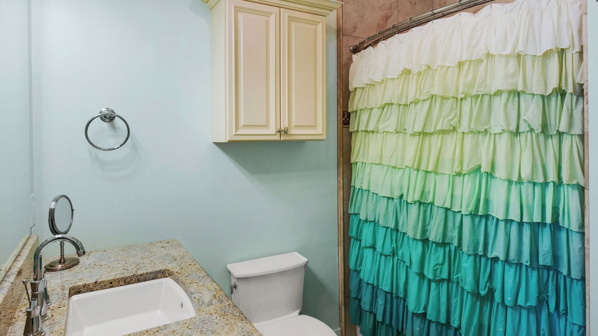 A bathroom with a sink, toilet, and a shower curtain with a ruffled design.