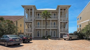 A multi-story building with a central entrance, a palm tree in front, and a brick driveway.