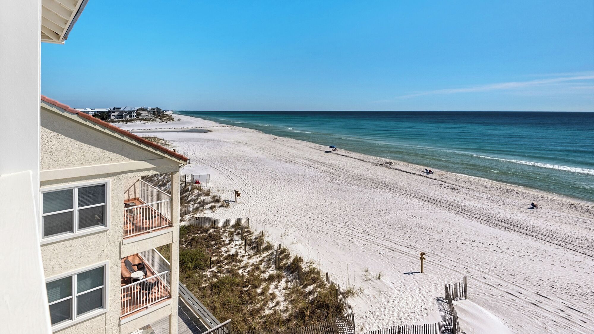 A beachfront property with a balcony overlooking the beach, a sandy walkway, and a view of the ocean.