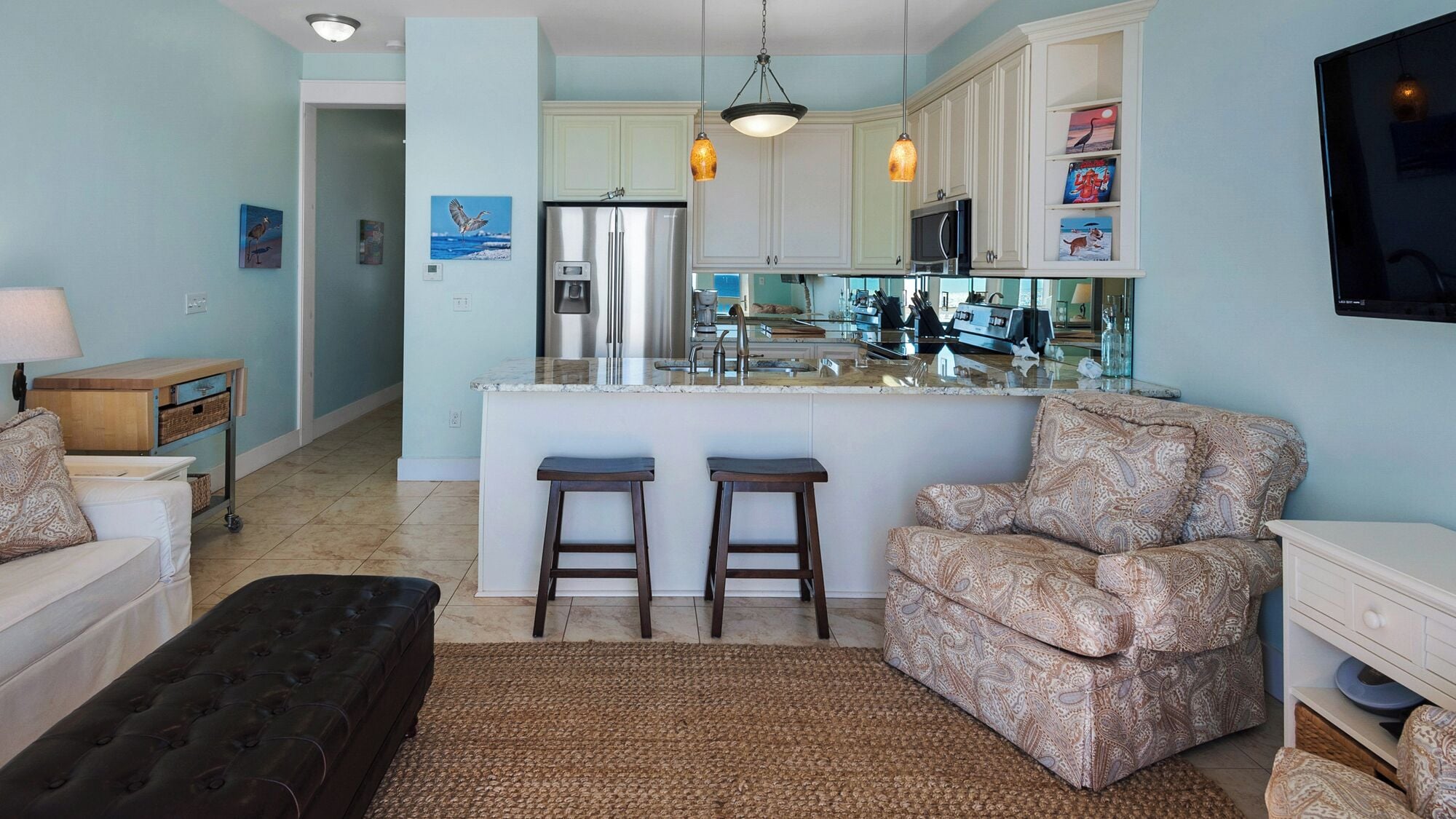 A modern kitchen with white cabinets, a central island with stools, and a dining area with patterned furniture.