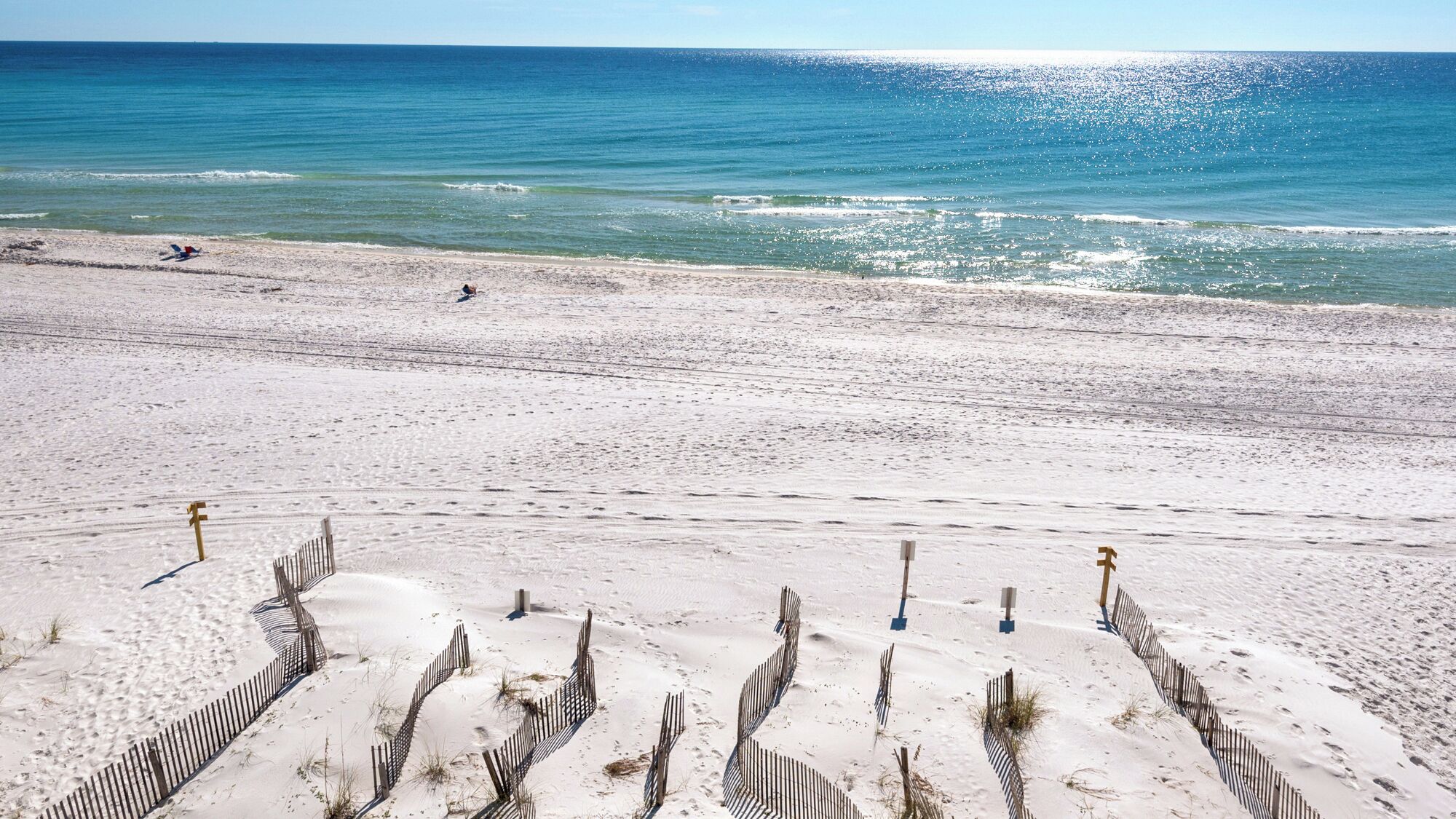 A sandy beach with a fence in the foreground and a clear view of the ocean.