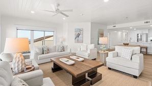 A spacious living room with a modern design, featuring a large window, a ceiling fan, and a kitchen area visible through an open door. - Gulf Front in Seagrove Beach With Sweeping Views (Santa Rosa Beach)