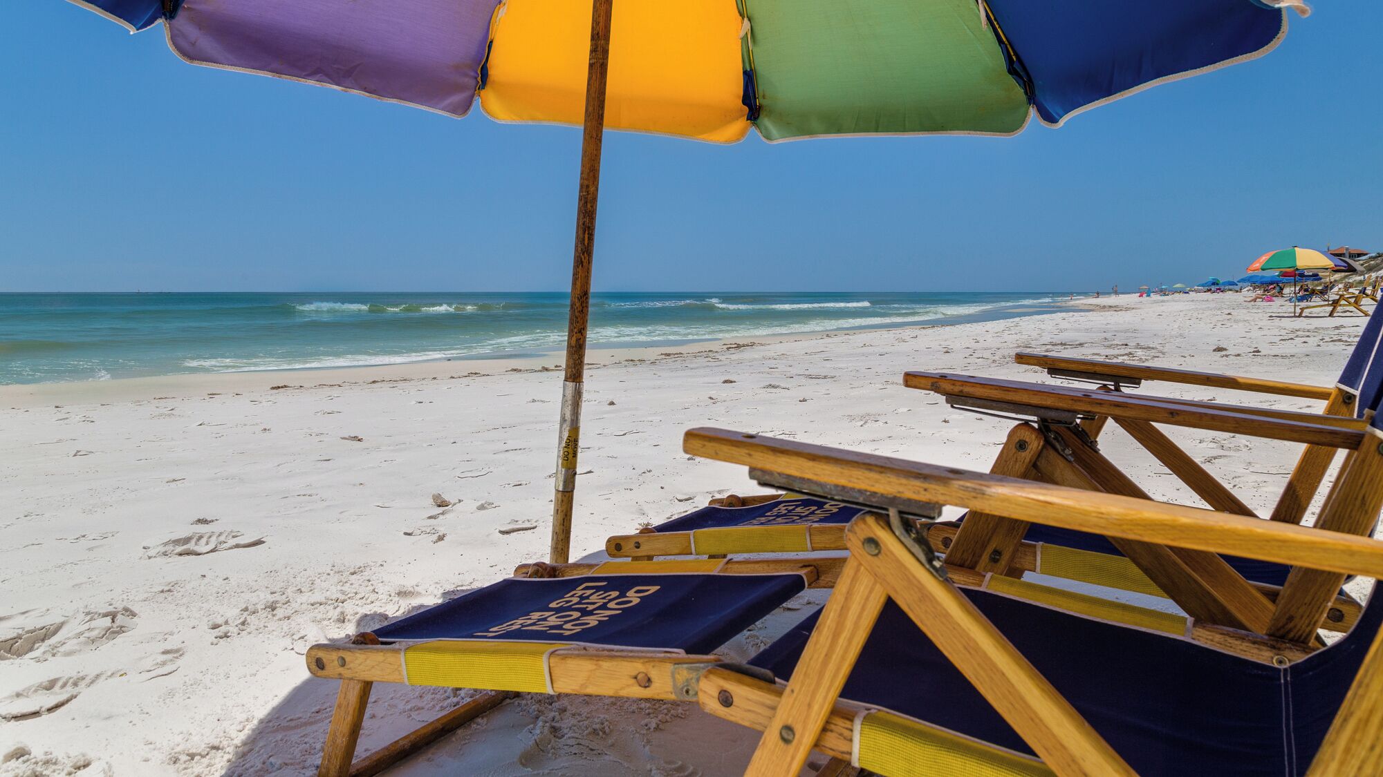 A beach with wooden lounge chairs and a colorful umbrella.