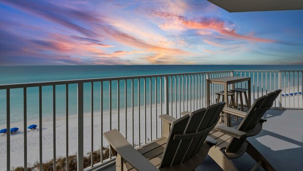 A balcony with two Adirondack chairs, a small table, and a view of the beach and ocean during sunset. - Gulf Front in Seagrove Beach With Sweeping Views (Santa Rosa Beach)