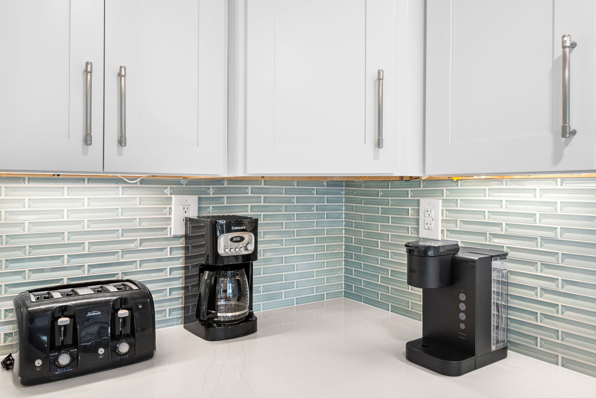 A kitchen with white cabinets, a toaster, a coffee maker, and a blender.