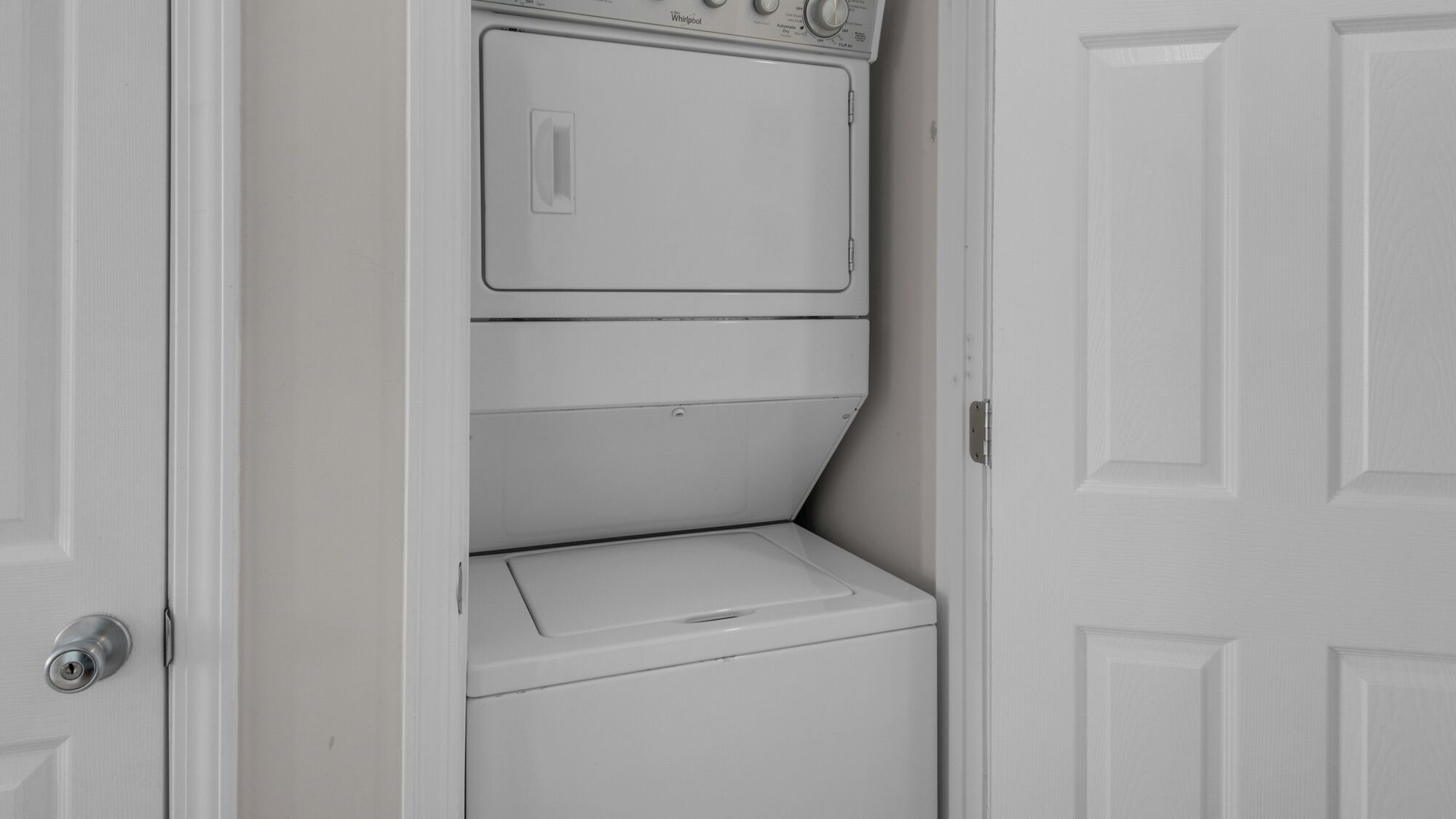 A white laundry room with a washer and dryer, a door, and a wall-mounted control panel.
