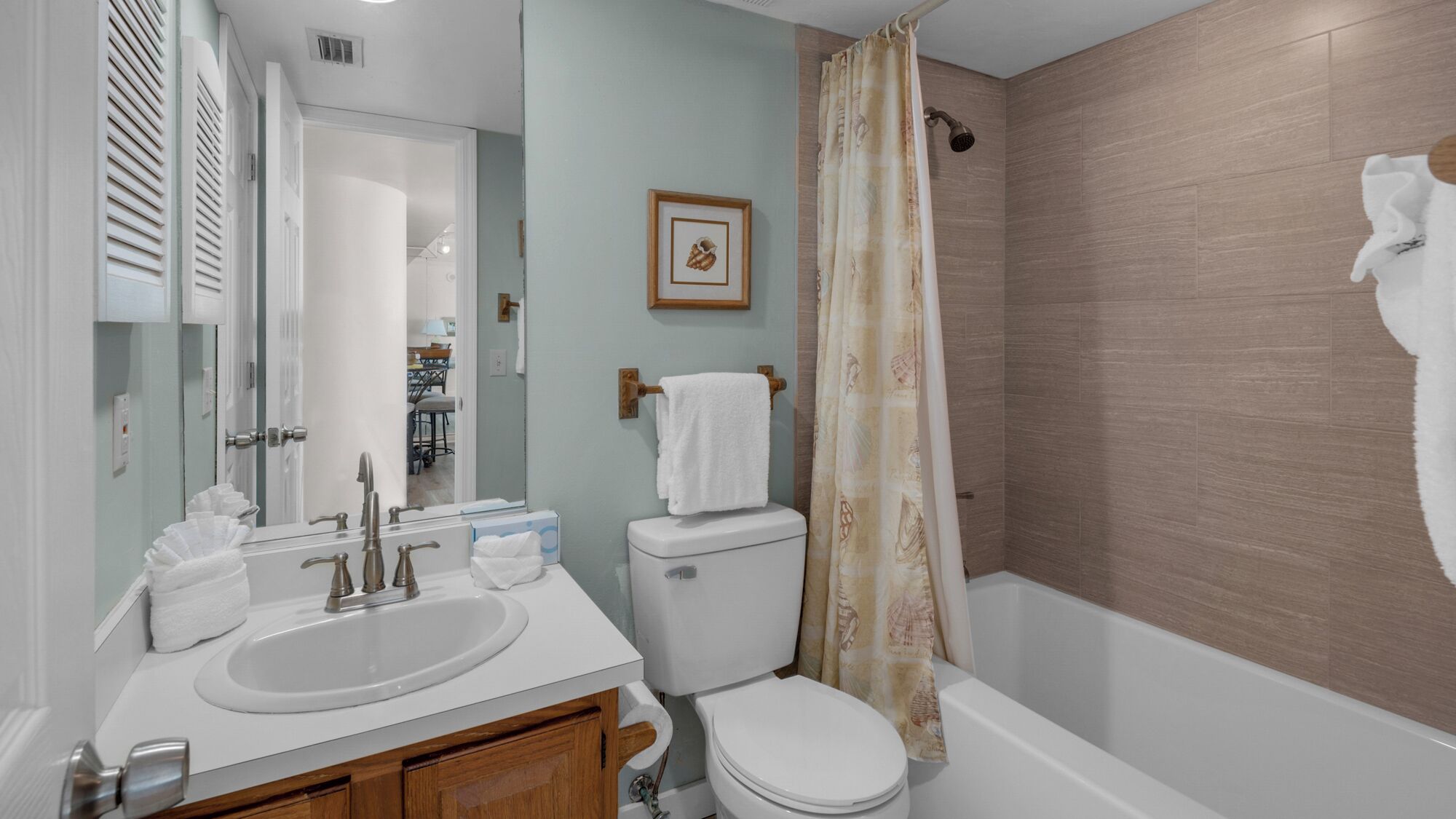 A bathroom with a sink, toilet, and shower. There is a framed picture on the wall and a towel rack with a towel.