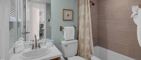 A bathroom with a sink, toilet, and shower. There is a framed picture on the wall and a towel rack with a towel.