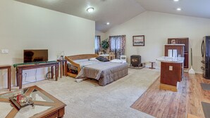 Een ruime woonkamer met een groot bed, een houten bijzettafeltje, een televisie en een open haard.