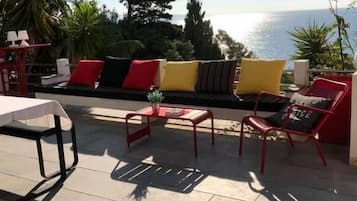 Une terrasse extérieure avec des meubles rouges, une table blanche et une vue sur la mer.