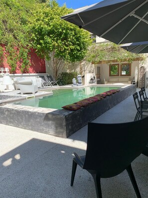 Un área de piscina con sillones de descanso, una mesa y sombrillas.
